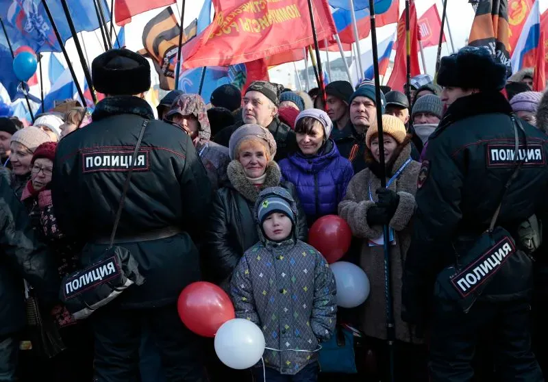 تجمع حاشد في شبه جزيرة القرم، يظهر فيه متظاهرون يحملون لافتات وأعلام، مع وجود أفراد من الشرطة بينهم طفل صغير.