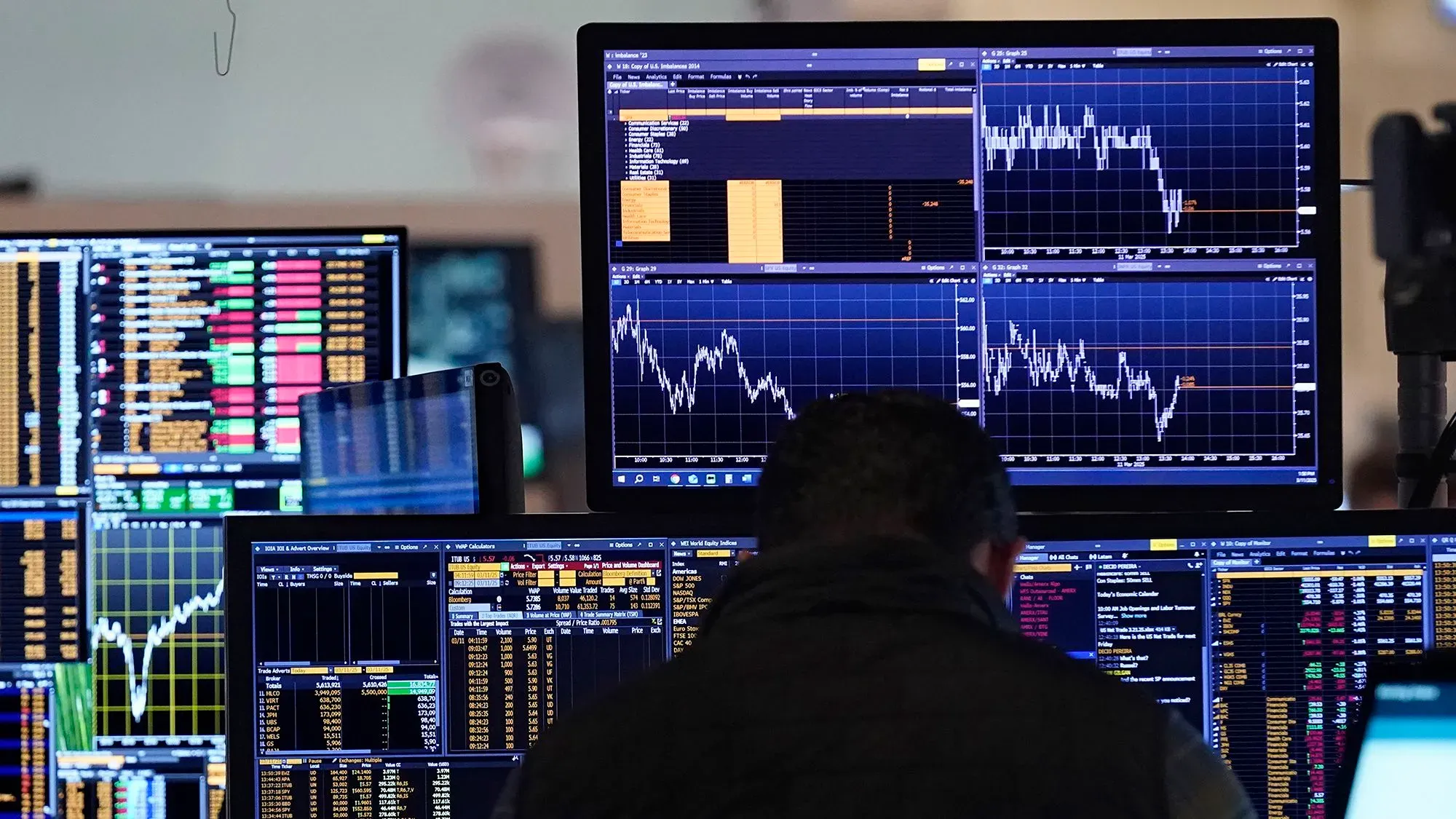 شخص يعمل على عدة شاشات تعرض بيانات سوق الأسهم، مع الرسوم البيانية والأرقام، مما يعكس الأوضاع الاقتصادية المتقلبة في فترة رئاسة ترامب.