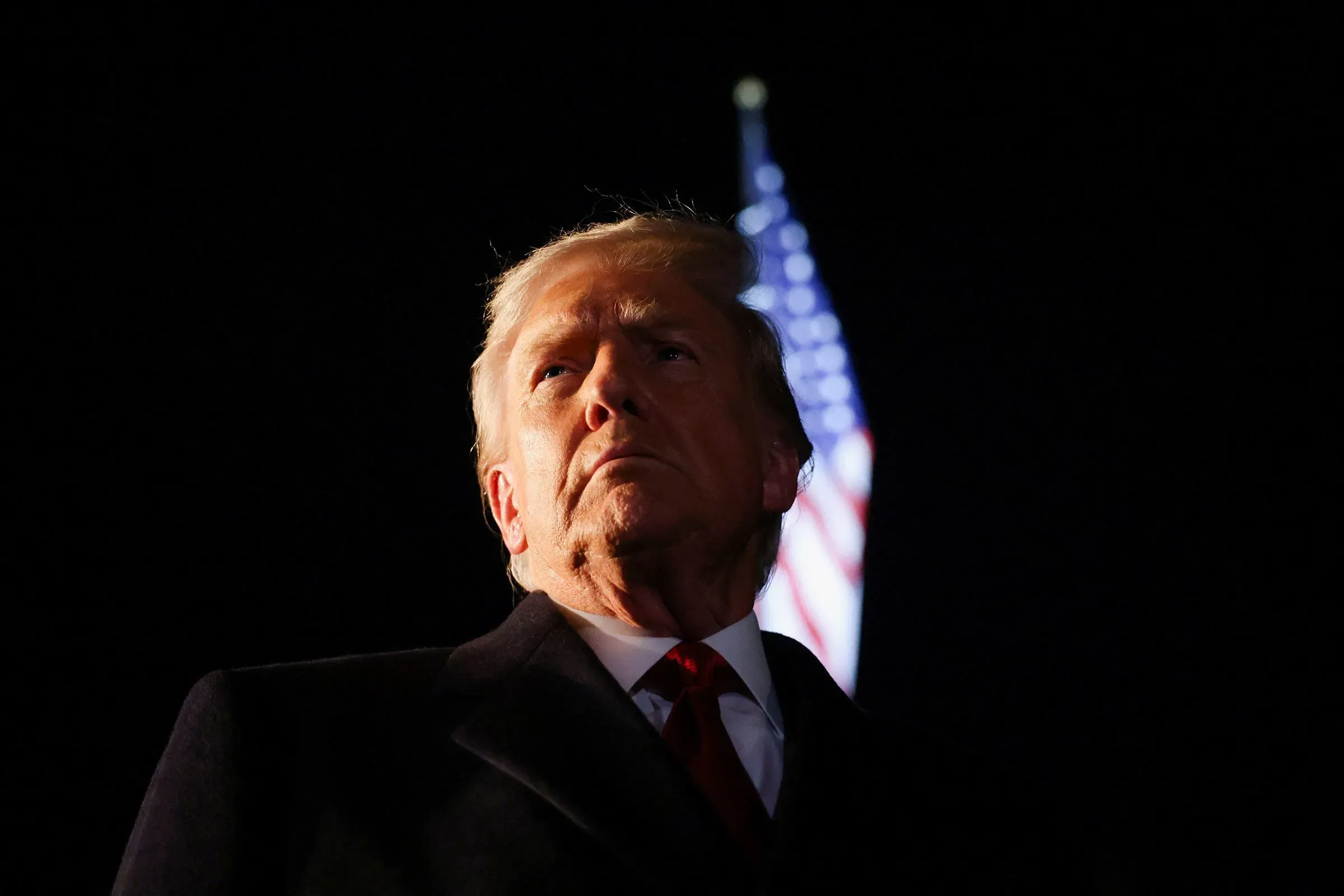 ترامب يتحدث بجدية، مع العلم الأمريكي في الخلفية، مع التركيز على تصريحاته حول الانتخابات الرئاسية وقيود التعديل الثاني والعشرين.