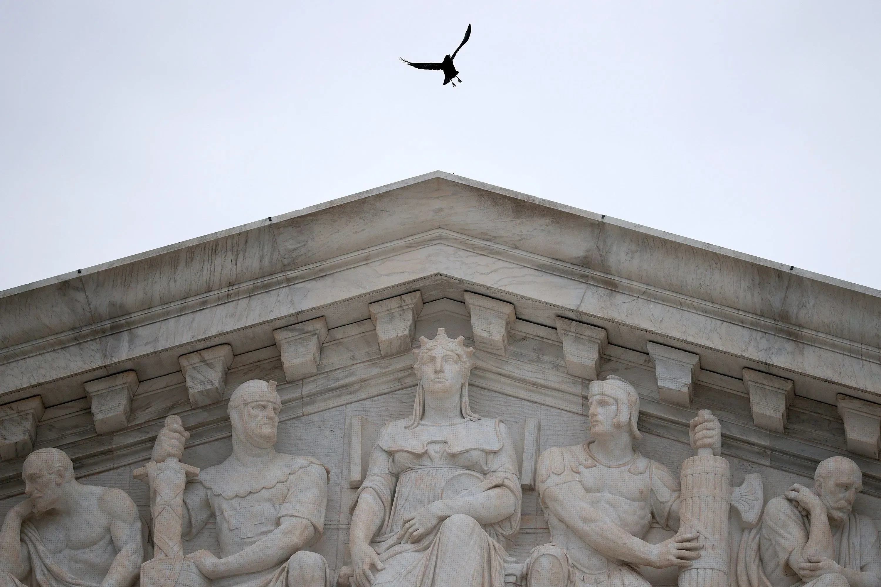 تمثال يمثل العدالة في قمة مبنى المحكمة العليا الأمريكية، مع طائر يحلق في السماء، مما يرمز إلى السلطة القانونية والرقابة.