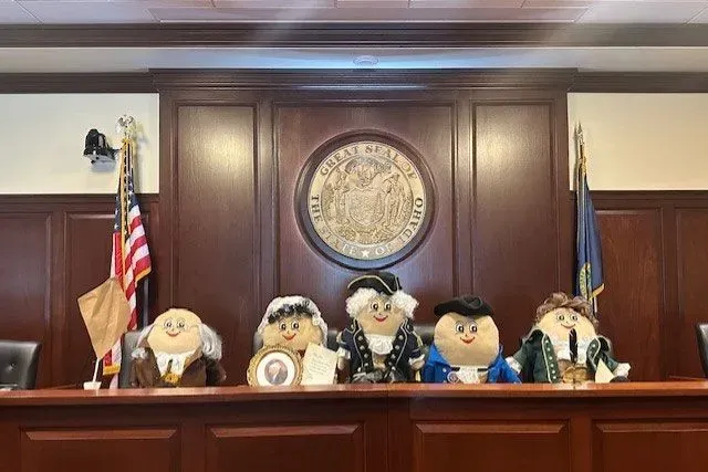 تمثال لخمسة شخصيات تاريخية أمريكية بأسلوب دمى في قاعة رسمية، مع شعار الدولة في الخلفية، يعكس الاحتفالات بالذكرى الـ250 لتأسيس الولايات المتحدة.