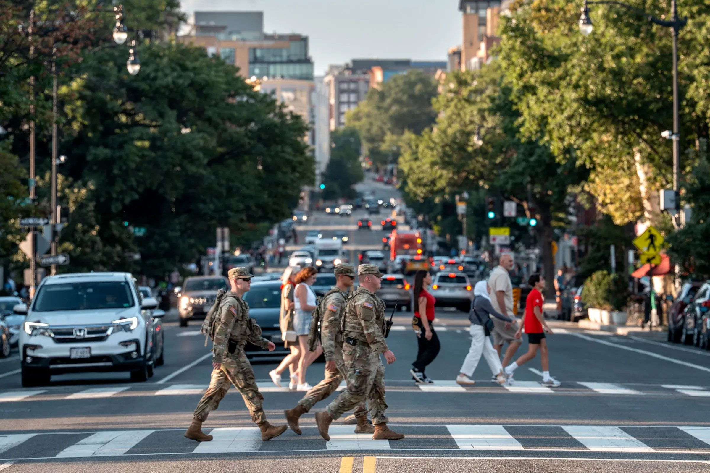 جنود من الحرس الوطني يعبرون الشارع في العاصمة واشنطن، محاطين بالمارة والسيارات، خلال أداء مهامهم اليومية.
