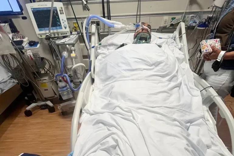 عامل مزارع مصاب في المستشفى بعد سقوطه خلال مداهمة لمزرعة في كاليفورنيا، مع وجود أجهزة طبية حوله.