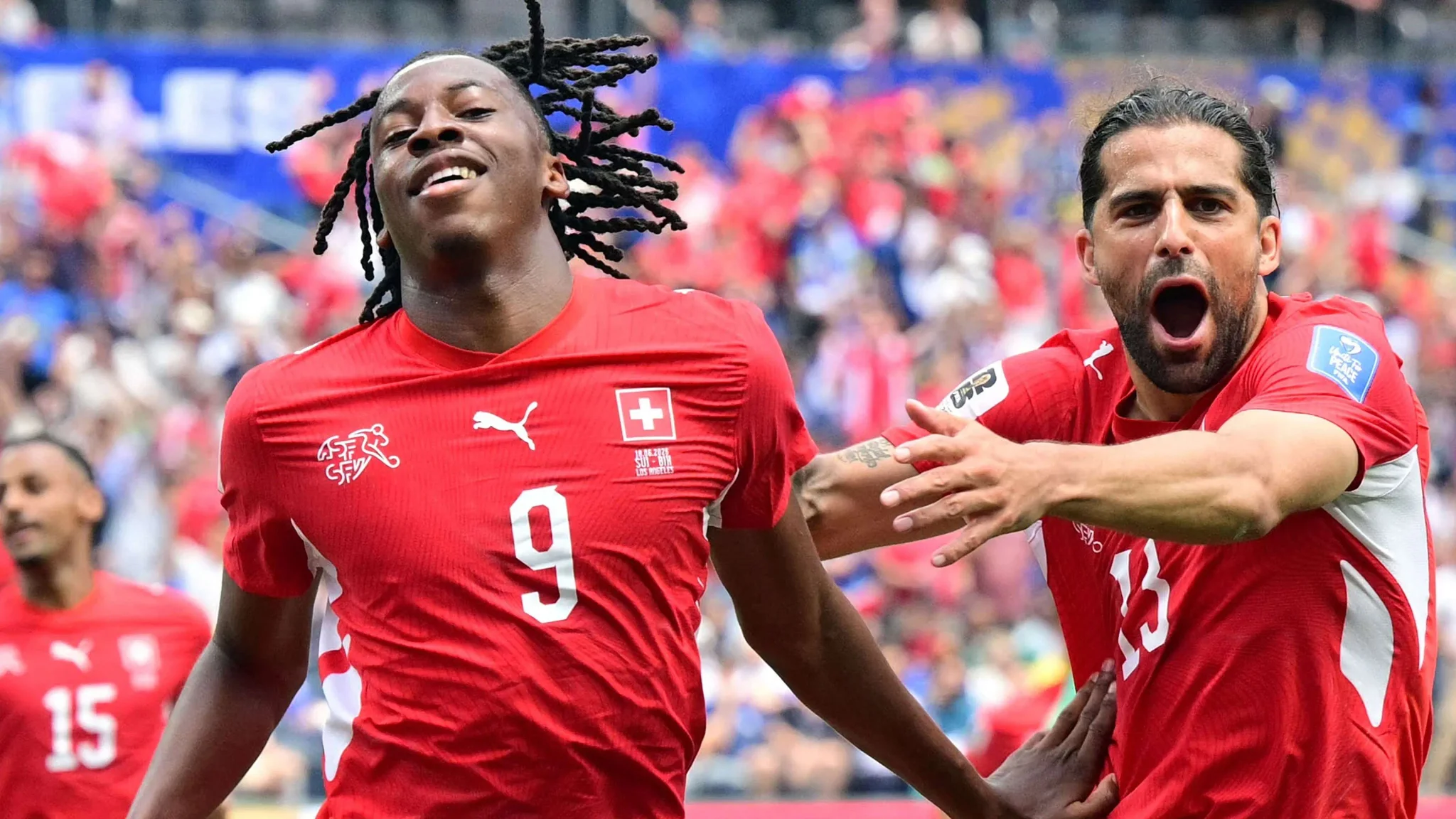 لاعب منتخب سويسرا رقم 9 يحتفل بهدفه بحماس مع زميله خلال مباراة في كأس العالم 2026، مع جمهور خلفهم في الملعب.