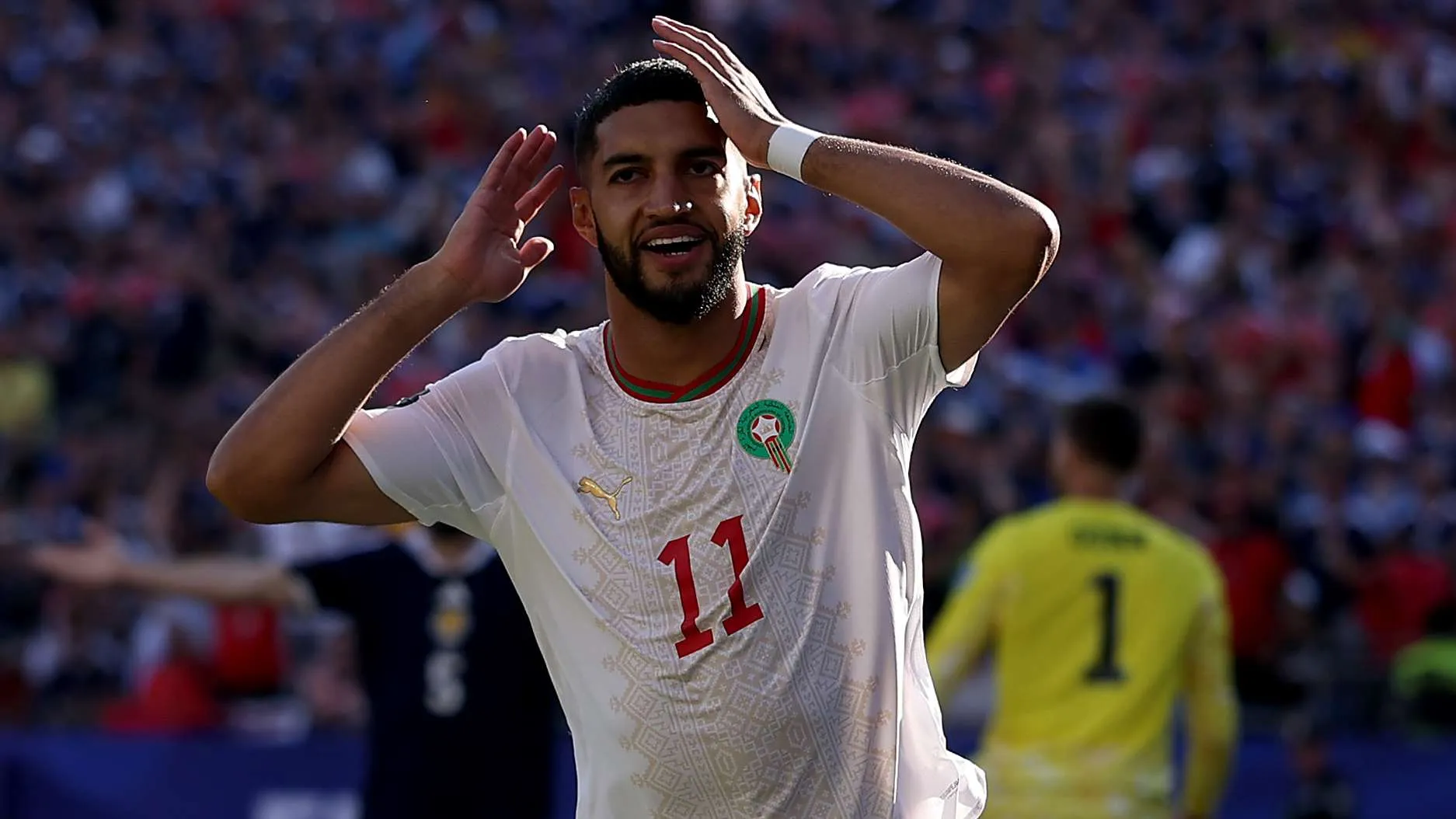 لاعب منتخب المغرب يرتدي الرقم 11 يحتفل بهدف في مباراة بكأس العالم 2026 وسط حشد جماهيري كبير في الملعب.
