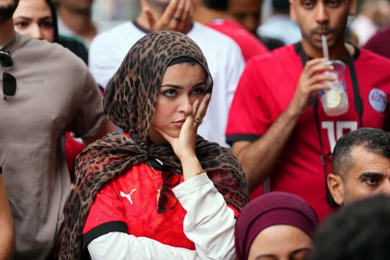 مشجعة مصرية تبدو حزينة وسط جمهور متأثر بخسارة منتخب مصر أمام الأرجنتين في كأس العالم والدور السادس عشر.