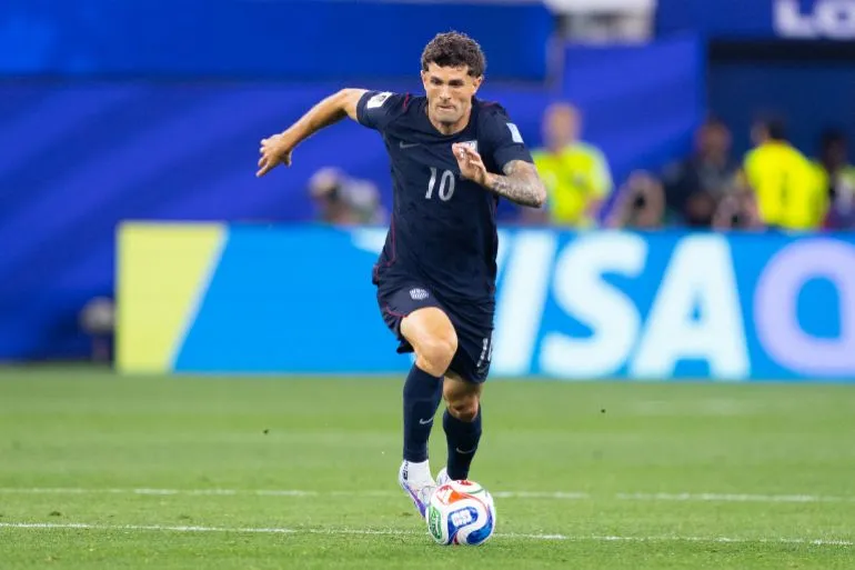 لاعب كرة قدم أمريكي يرتدي القميص رقم 10، يركض بسرعة خلال مباراة في كأس العالم، مع خلفية تظهر شعار الفيفا.