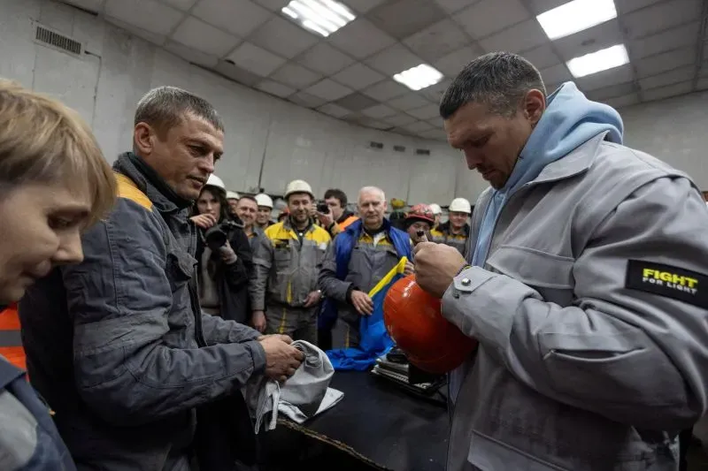 أولكسندر أوسيك، بطل الوزن الثقيل، يوقع على خوذة لأحد العمال في مركز عمل مشترك، محاطاً بمجموعة من الأشخاص الذين يرتدون زي العمل.