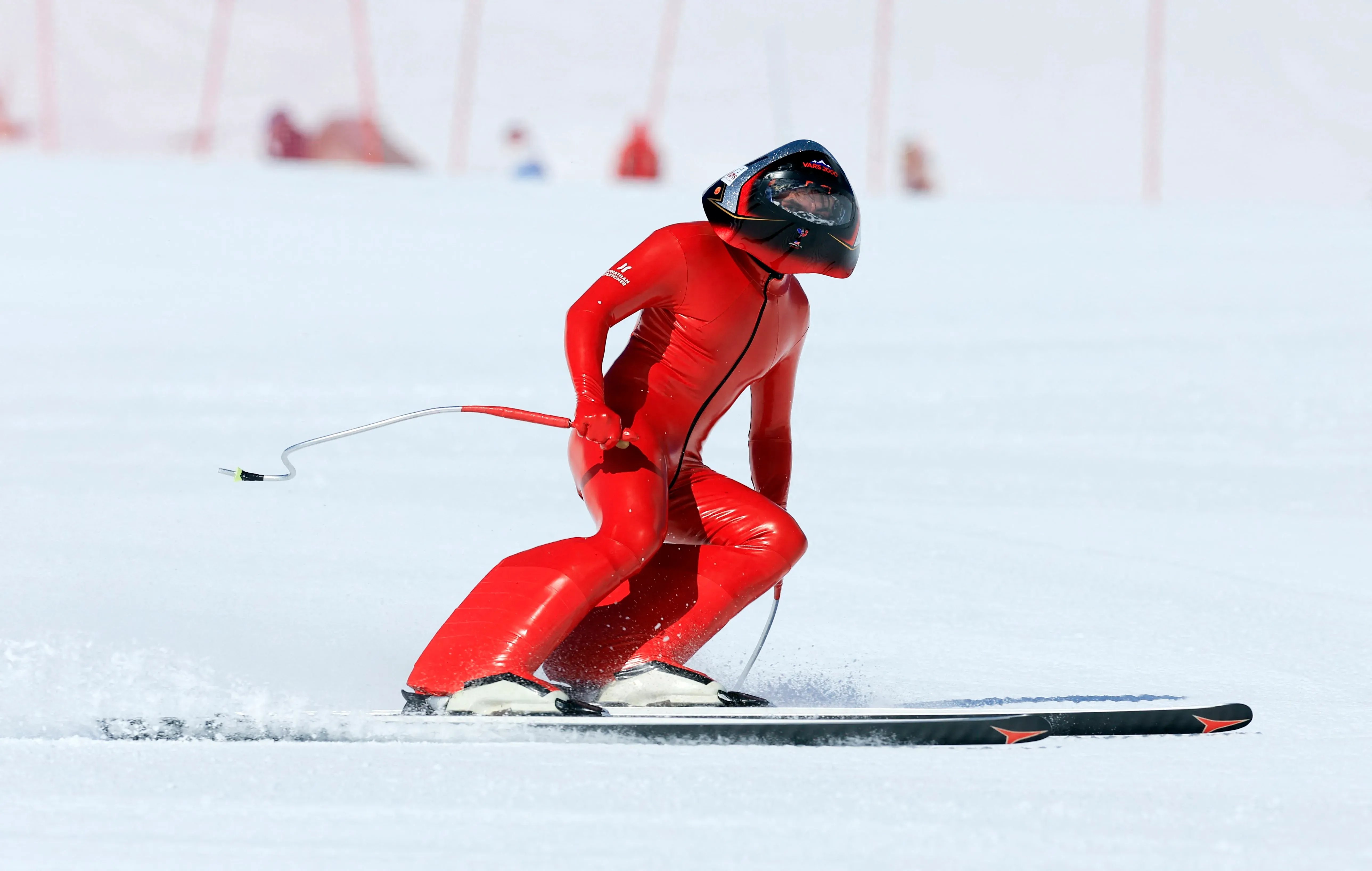 متزلج يرتدي بدلة حمراء وزلاجات، ينطلق بسرعة على منحدر ثلجي، مع خوذة داكنة، معبراً عن شغفه بالتزلج السريع وتحقيق الأرقام القياسية.