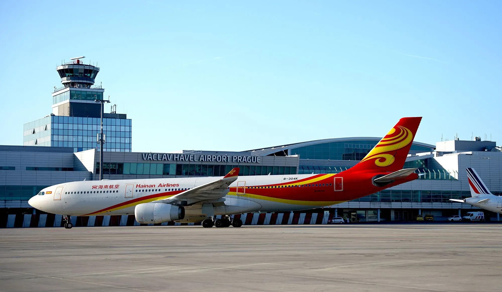 طائرة تابعة لشركة طيران هاينان متوقفة في مطار فاتسلاف هافل ببراغ، مع برج المراقبة والمباني الحديثة في الخلفية.