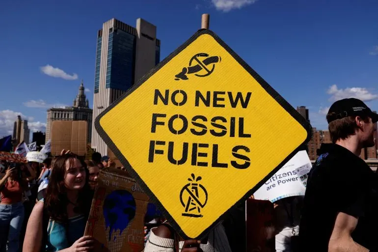 لا لوقود الأحفوري الجديد، لافتة صفراء تحمل رسالة قوية ضد مشاريع الطاقة الأحفورية، مع حشد من المتظاهرين في الخلفية.