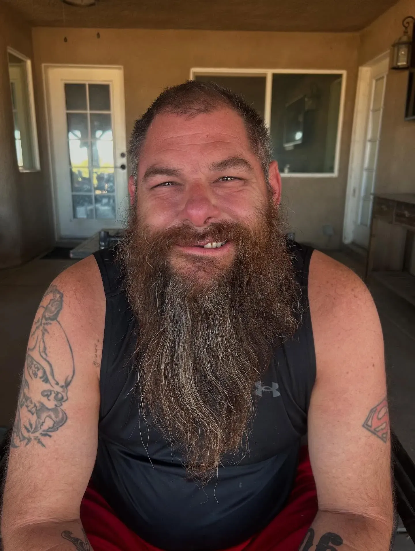 ابتسامة رجل ذو لحية كثيفة، يجلس في مكان داخلي، مع خلفية تحتوي على نوافذ وأبواب زجاجية، بعد تعرضه لإصابات في حادث مصارعة.