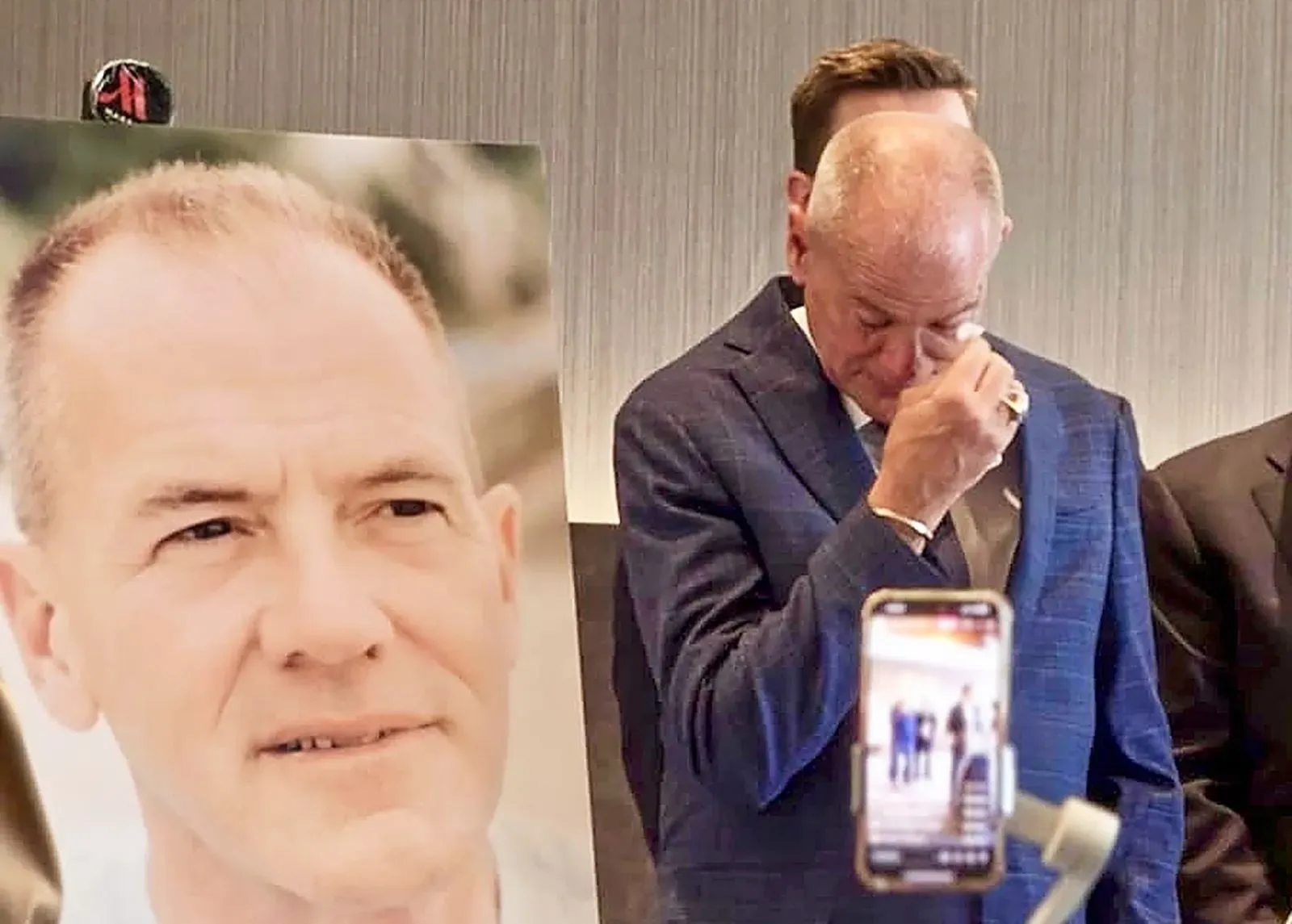 رجل يتأثر عاطفياً أثناء حديثه عن قضيته بعد 32 عاماً من السجن ظلماً، مع صورة له خلفه، في مؤتمر صحفي حول التعويضات.