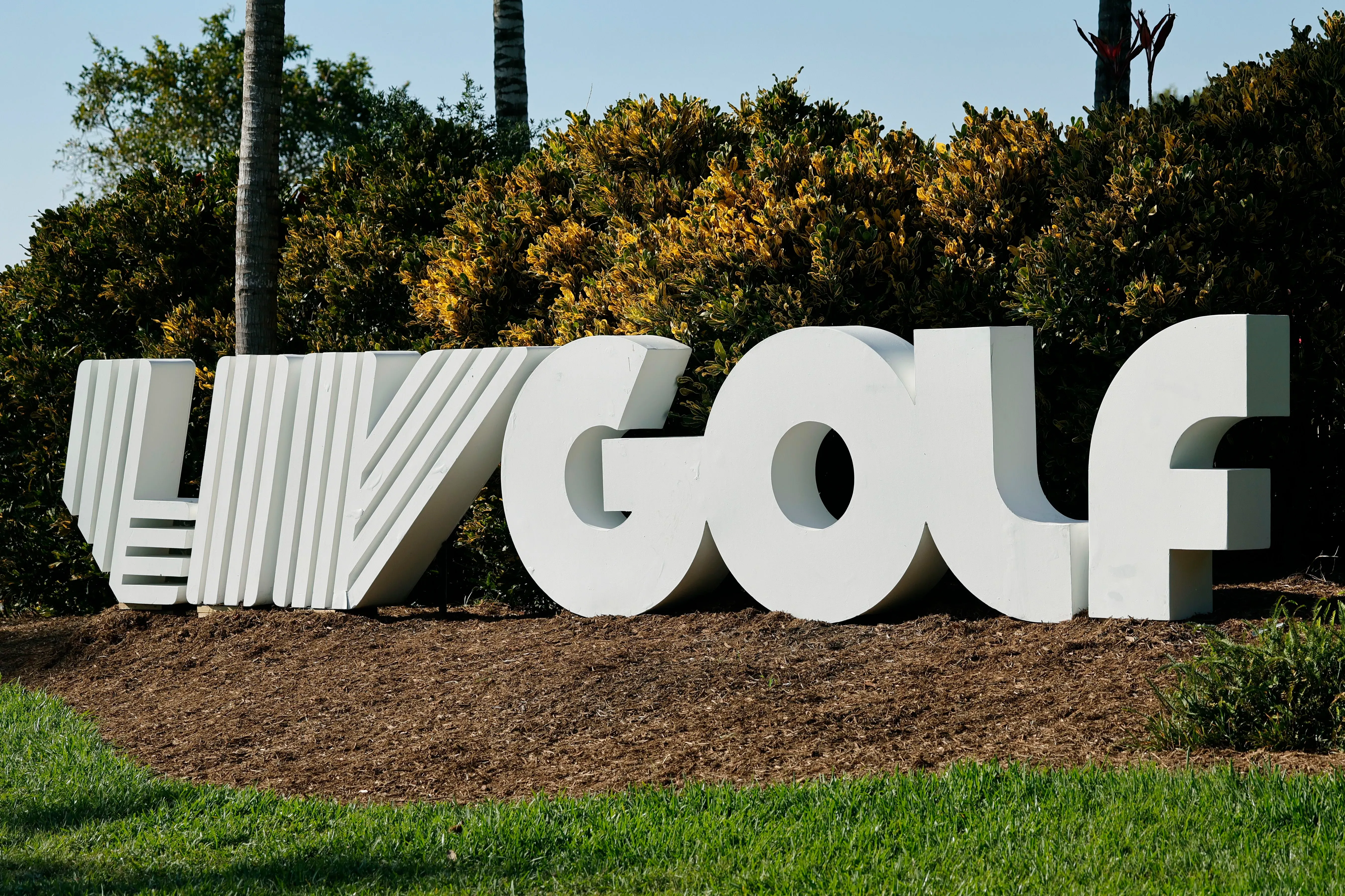 شعار دوري LIV Golf يظهر في موقع خارجي محاط بالنباتات، مع التركيز على التحديات المالية والتهديدات التي يواجهها الدوري.