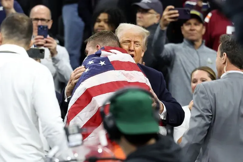 هندريكسون يحتفل بفوزه في بطولة المصارعة الوطنية مع الرئيس ترامب، مغطىً بالعلم الأمريكي، وسط حماس الجمهور بعد انتصاره المفاجئ.