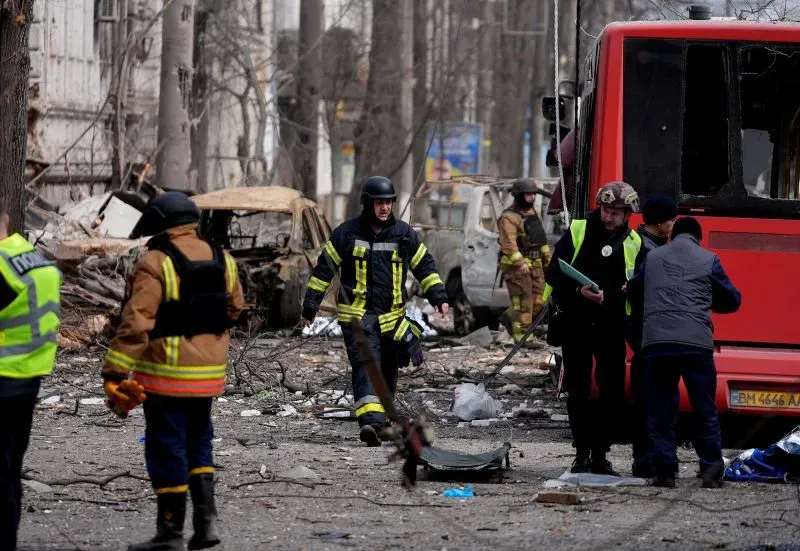 رجال إطفاء وفرق إنقاذ يعملون في موقع دمار شديد، مع وجود مركبات مدمرة وخلفية من الأشجار، في سياق النزاع الأوكراني.