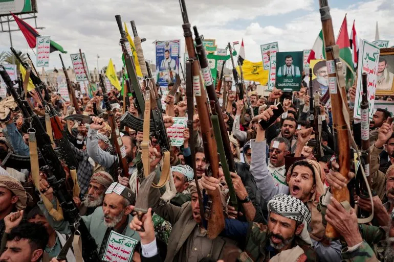 مسلحون حوثيون يرفعون أسلحتهم ويهتفون في مظاهرة احتجاجية تعبر عن التوترات والصراع المستمر في اليمن.