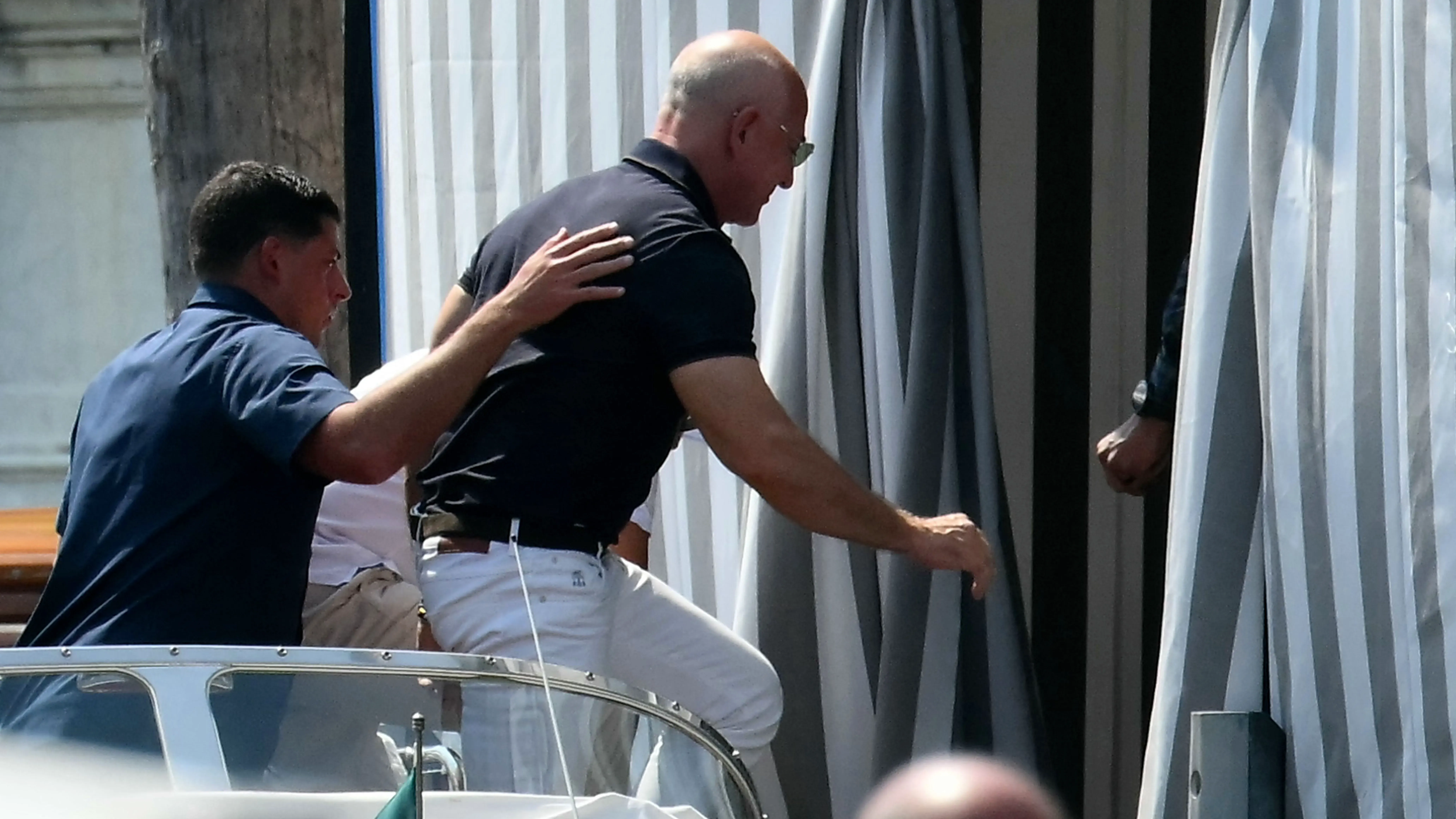 جيف بيزوس يتجه نحو مدخل مع حارسه الشخصي، بينما تتدلى ستائر مخططة خلفهم، مما يعكس أجواء حفل زفافه.