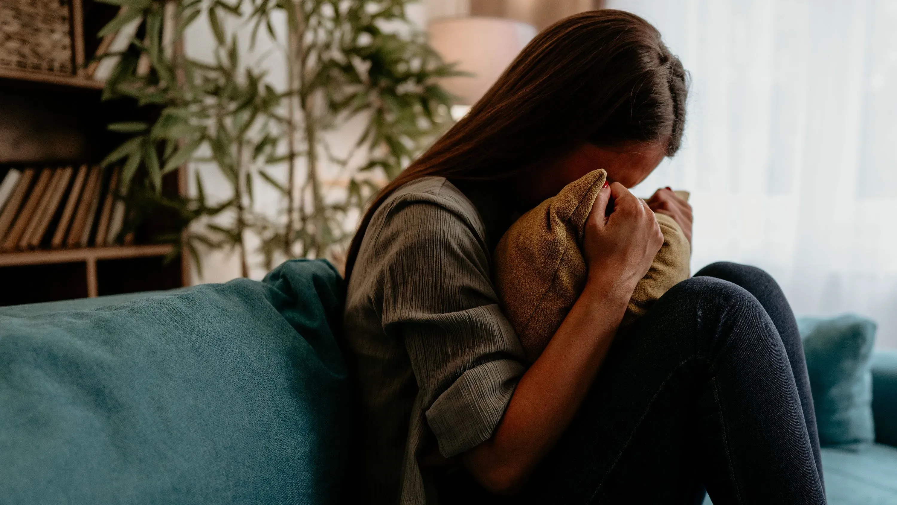 امرأة تجلس على الأريكة تحتضن وسادة، تعبر عن الحزن العميق بعد فقدان أحد أحبائها، مما يعكس تأثير الفجيعة على الصحة النفسية.