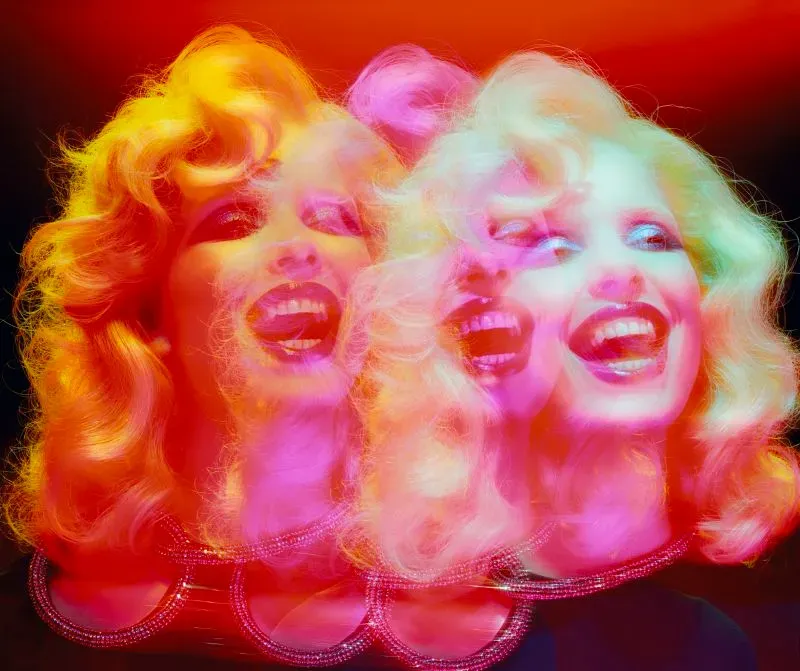 صورة ملونة لامرأة ذات شعر أشقر مجعد تضحك، مع تأثيرات ضوئية متعددة تعكس جوانب سينمائية، تعبر عن أسلوب مايلز ألدريدج الفريد.
