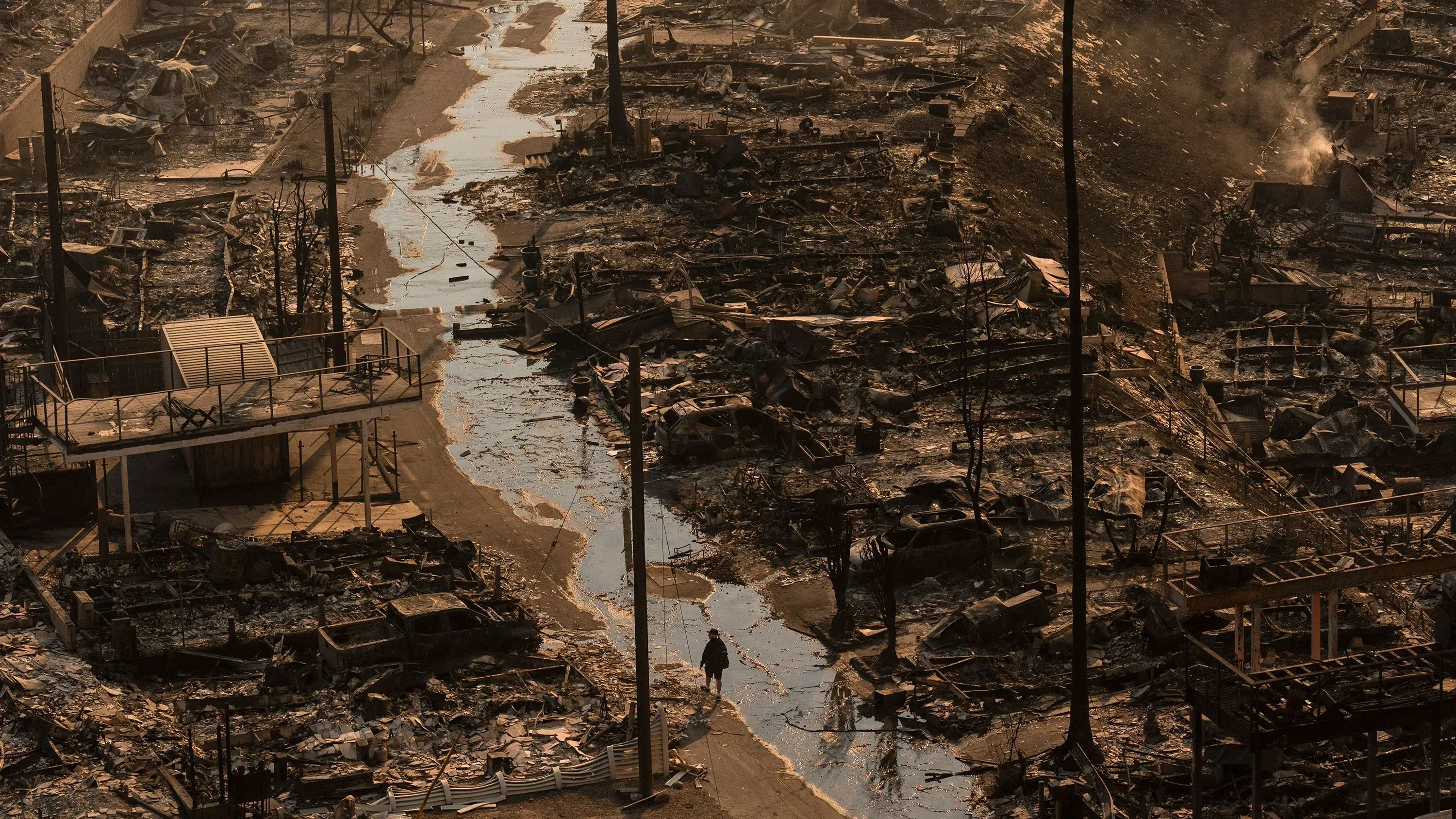 مشهد لمدينة مدمرة بعد حرائق الغابات، مع دمار شامل للمباني والطرق. تظهر آثار الكارثة على المنازل وتأثيرها على التأمين.