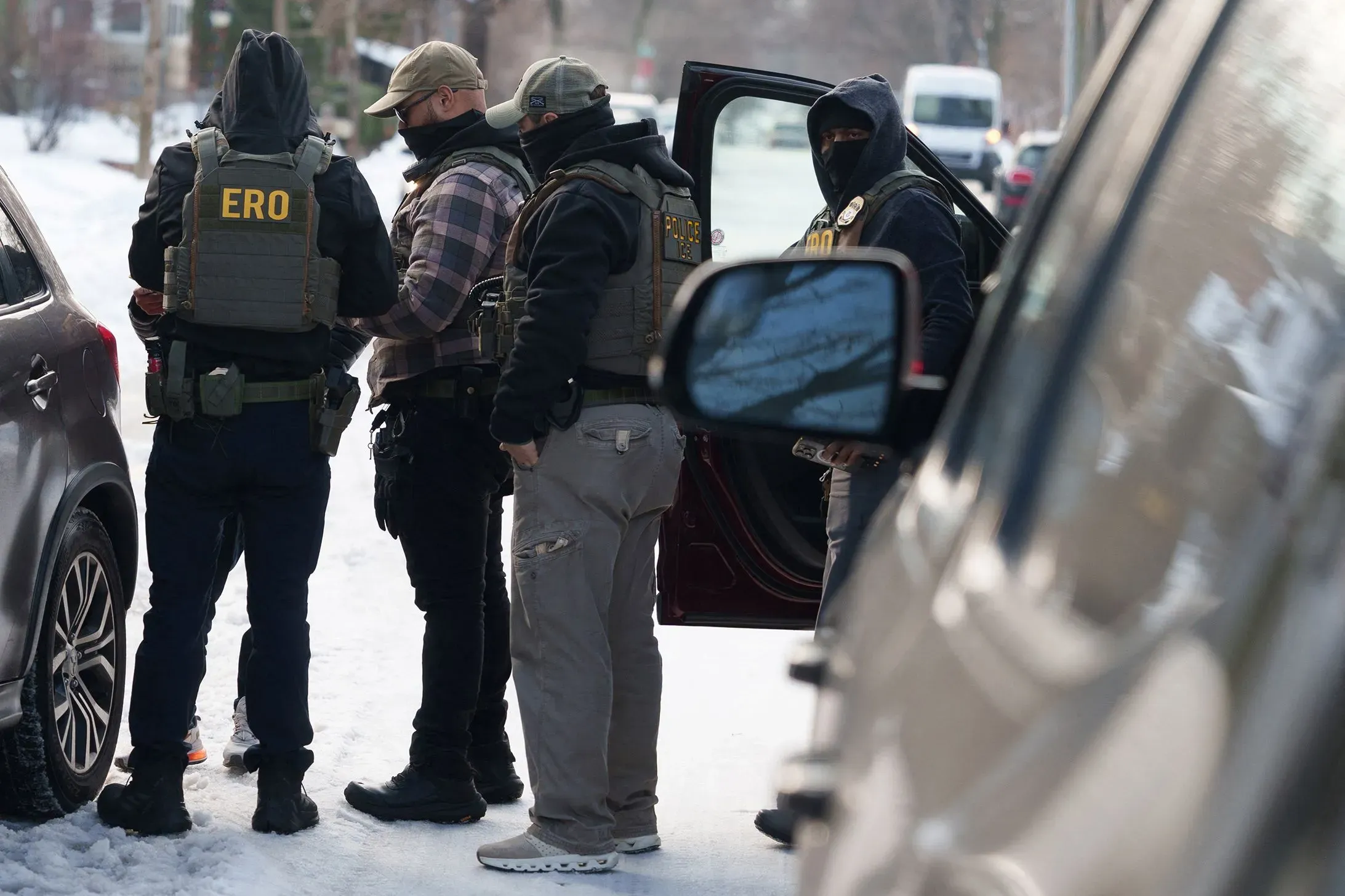 عملاء فيدراليون يرتدون سترات واقية يتجمعون في منطقة ثلجية، مع التركيز على تنفيذ عمليات التحقق من الهوية في مينيابوليس.