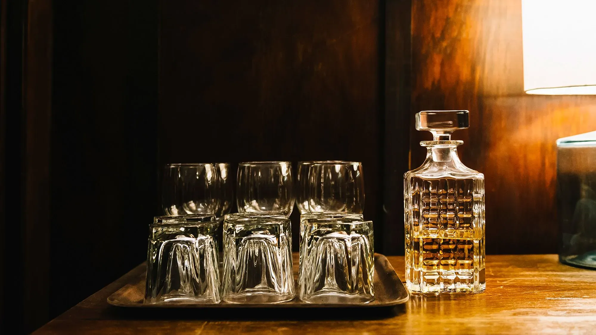 زجاجة كحولية مع مجموعة من الكؤوس على صينية، تعكس تقليد تناول المشروبات المسائية وتأثيرها على النوم وجودته.