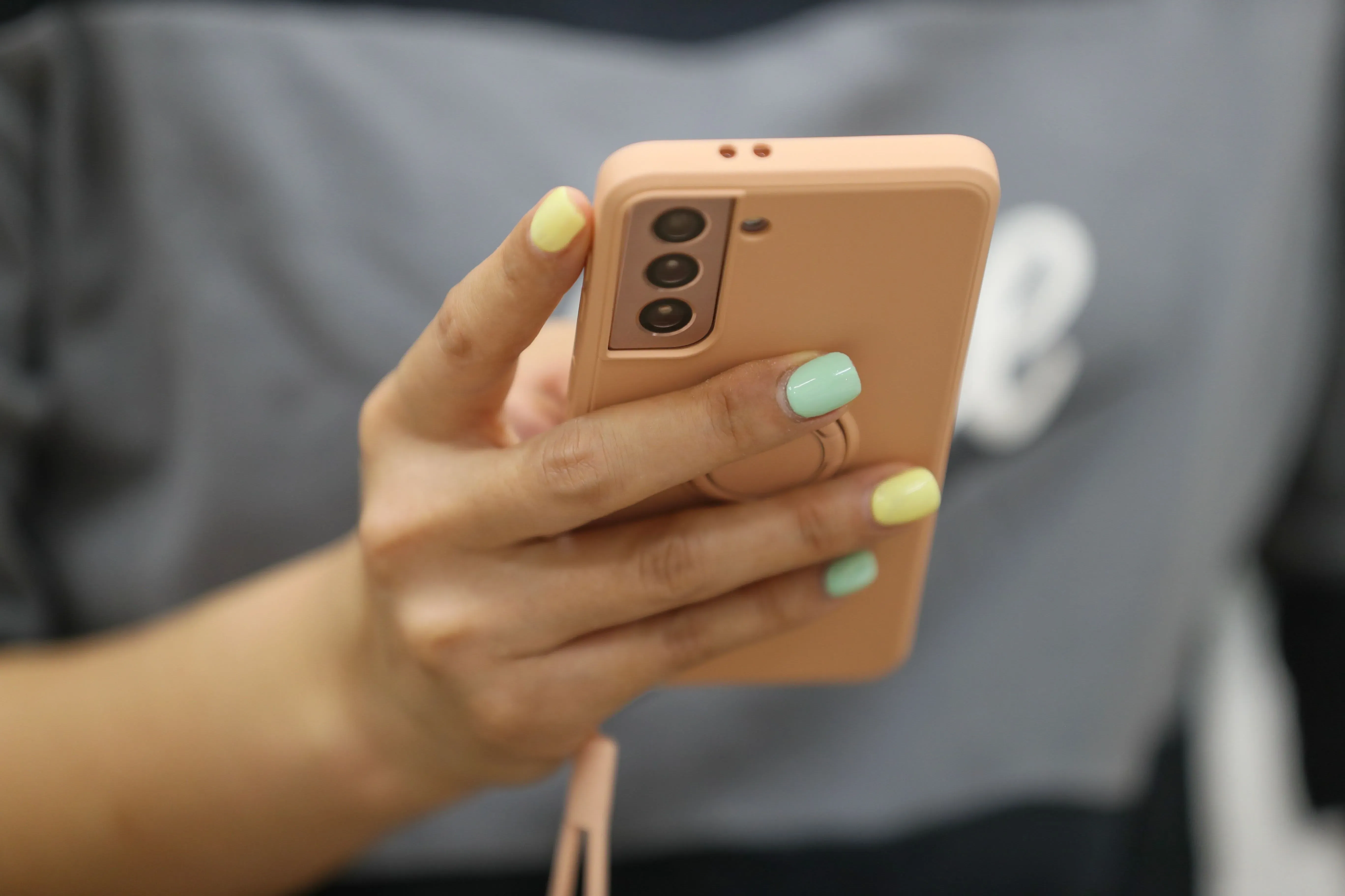 يد تحمل هاتفًا ذكيًا بلون وردي، تظهر أظافر ملونة بألوان زاهية، تعكس اهتمامًا بالتكنولوجيا ووسائل التواصل الاجتماعي.