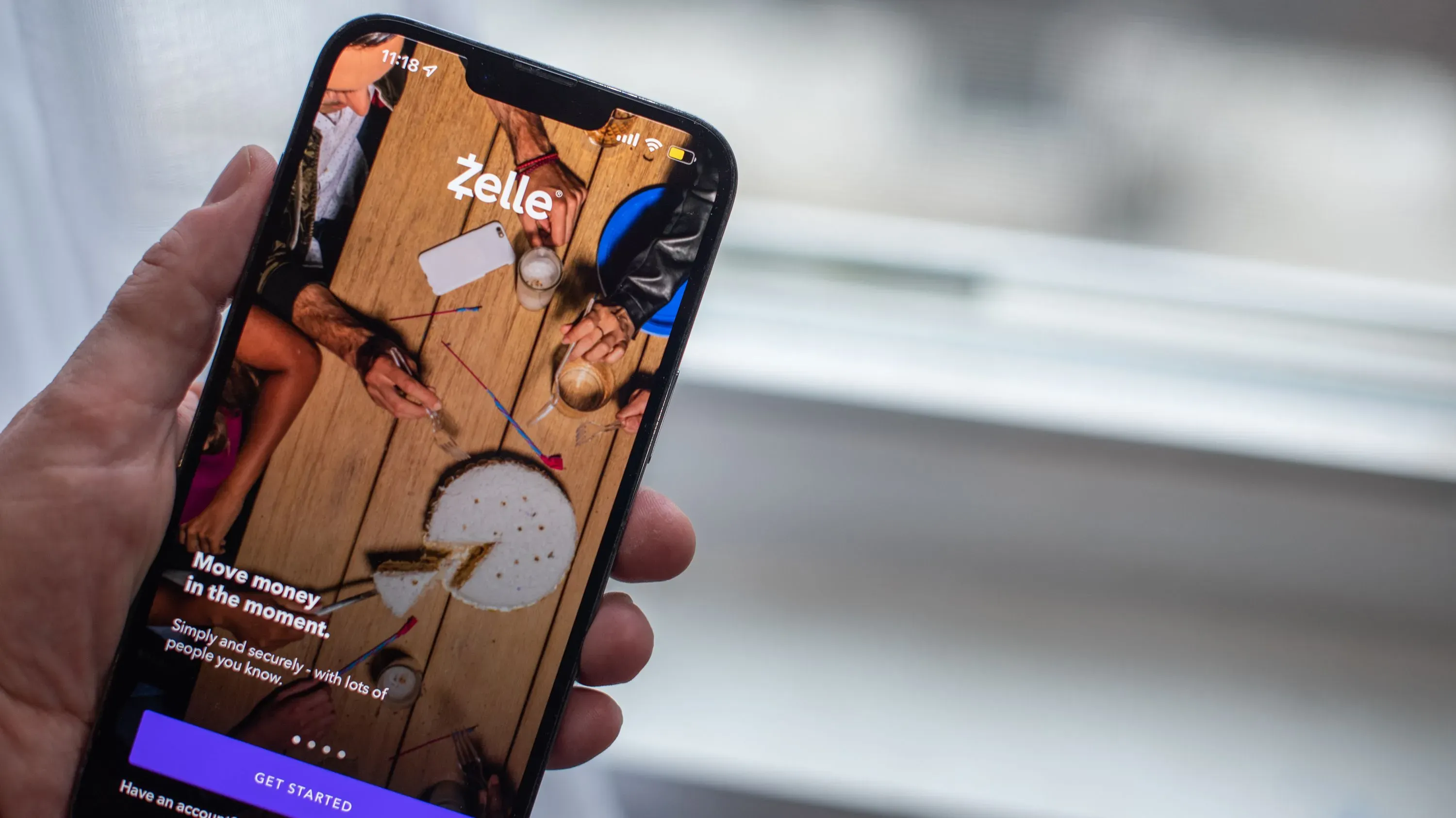تطبيق Zelle مفتوح على هاتف ذكي، يعرض واجهة المستخدم مع خيارات لتحويل الأموال بين الأفراد، محاط بأدوات وأكواب.