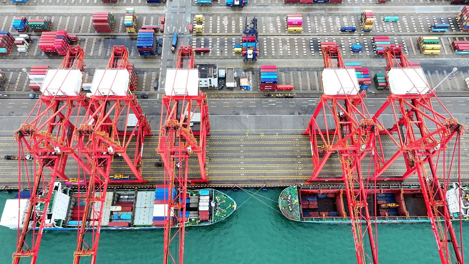 انخفاض حركة الشحن في ميناء مزدحم، مع سفن حاويات راسية في الميناء ورافعات حمراء، مما يعكس تأثير الحرب التجارية بين الولايات المتحدة والصين.