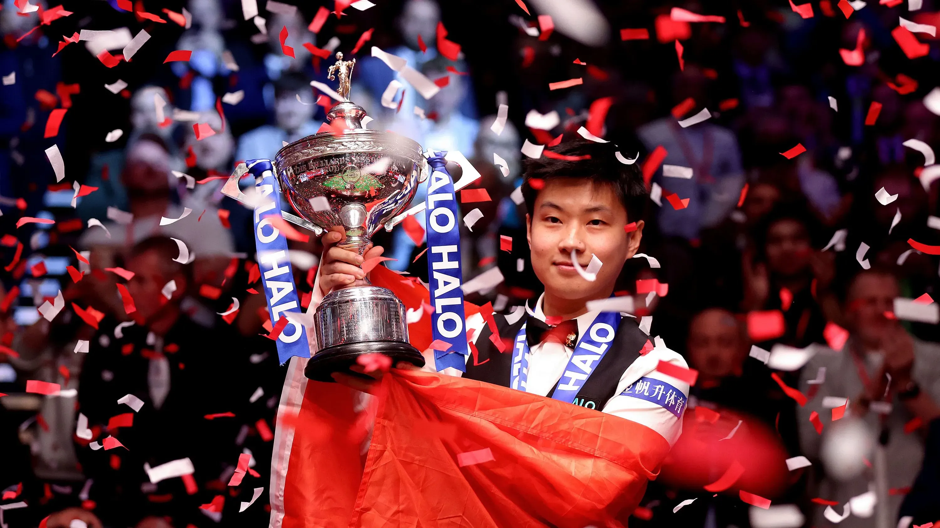 تشاو شينتونج يحمل كأس بطولة العالم للسنوكر، محاطًا بأوراق ملونة، بعد فوزه التاريخي على مارك ويليامز في كروسيبل.